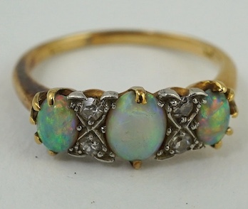 A yellow metal (stamped 18) and three stone white opal set half hoop ring, with diamond chip spacers, size M, gross weight 3.1 grams. Condition - poor to fair